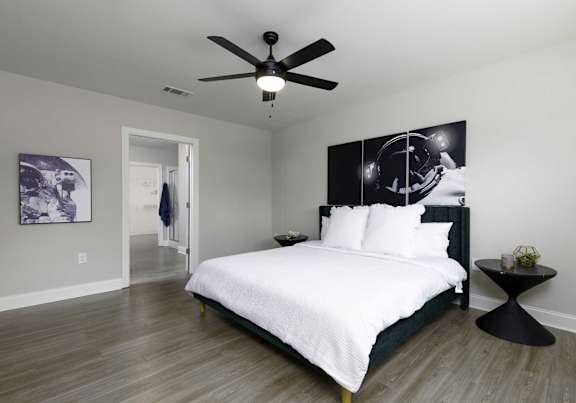 A bedroom with a bed, a ceiling fan, and a wall art.