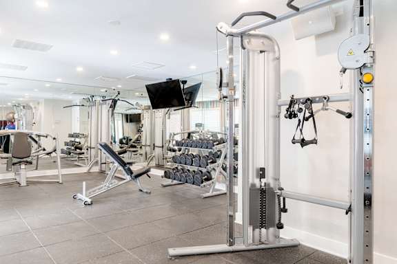A gym with a variety of equipment including a weight bench, a cable machine, and a flat screen TV.