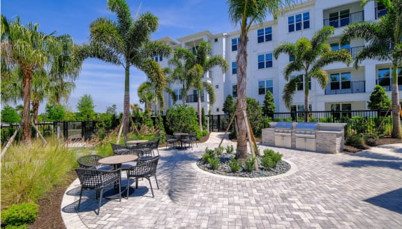 a patio with tables and chairs and palm trees in front of a building at Altis Grand Lake Willis, Orlando Florida