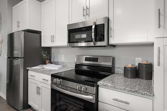 A black refrigerator and oven in a kitchen with white cabinets.