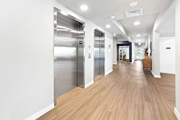 A long hallway with wood floors and two elevators.