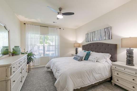 A bedroom with a large bed, a dresser, and a ceiling fan.