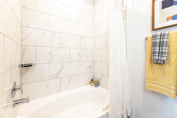 A white bathroom with a marble tile wall and a white bathtub.
