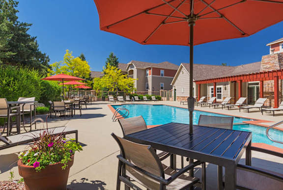 A poolside table with chairs and an umbrella overlooking a pool.