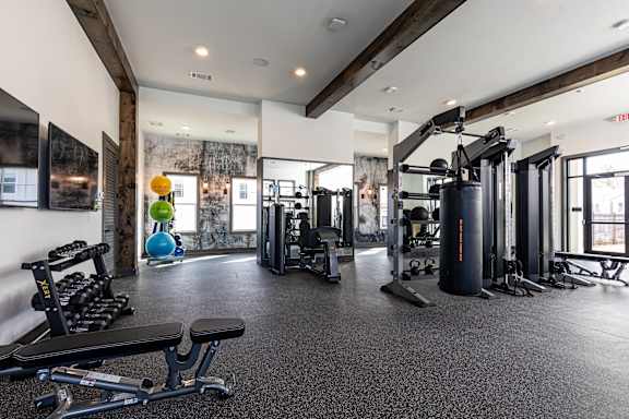 A gym with a variety of equipment including a squat rack, dumbbells, and a bench.
