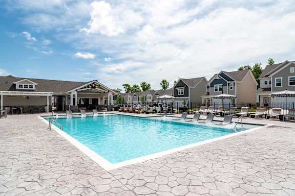 A large swimming pool surrounded by a stone patio and houses in the background.