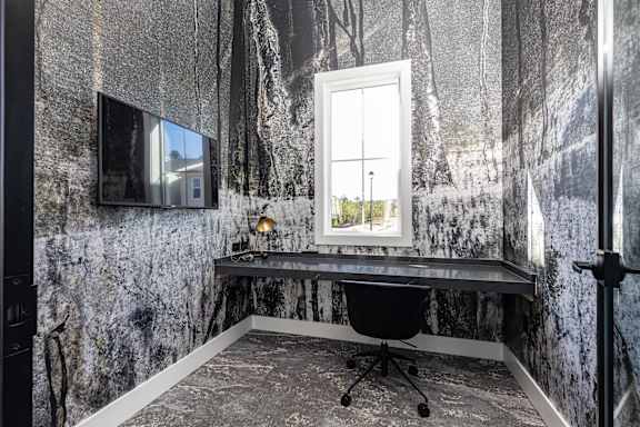 A black chair is in front of a desk with a lamp on it.