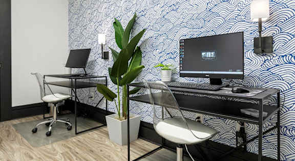A black and white patterned wall behind a desk with a laptop and a monitor on it.