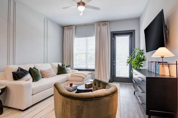A living room with a white couch, a brown armchair, and a flat-screen TV mounted on the wall.