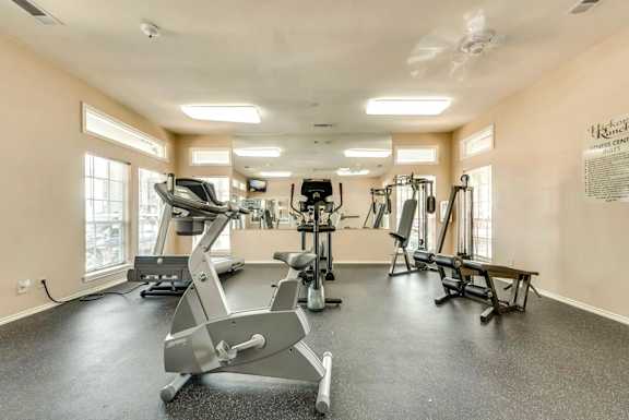 A spacious gym with various exercise equipment and a fan on the ceiling.