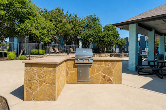 A stone barbecue grill is in the middle of a concrete patio.