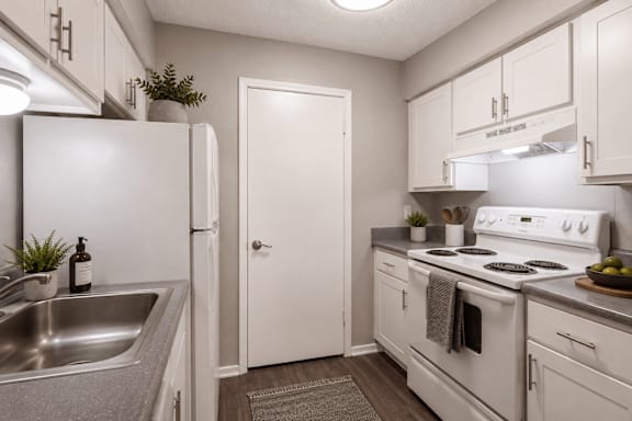 A white kitchen with a sink, refrigerator, and stove.