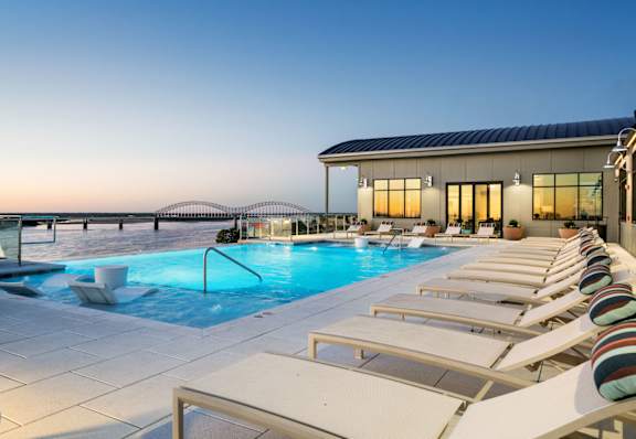 A pool with sun loungers and a building in the background.