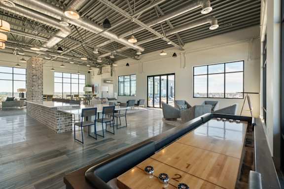 A shiny wooden table with four legs and four wheels is in the middle of a room with a brick pillar and a window.