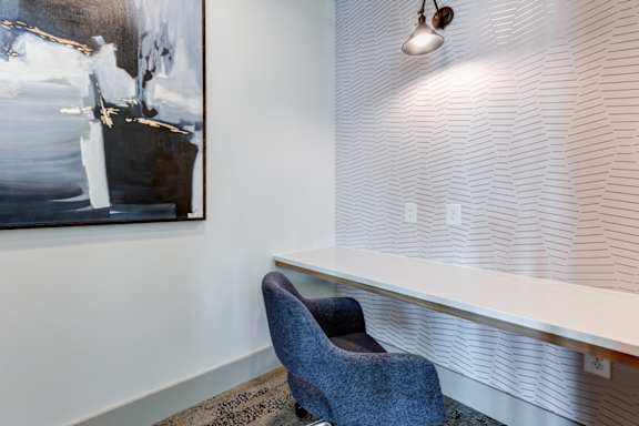 A blue chair sits in front of a wall with a painting and a light.