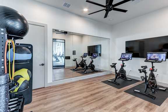 A room with a mirror, a fan, and exercise bikes.