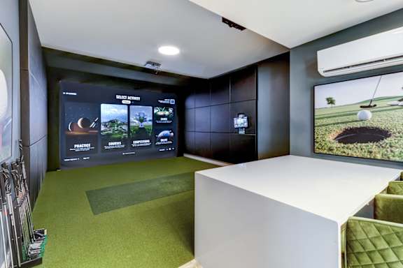 A room with a golf simulator and a green screen.
