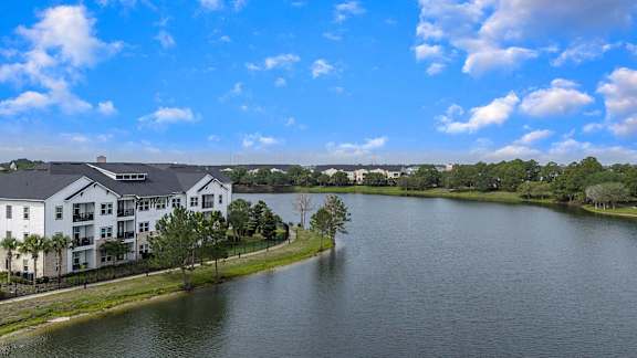 A large white building is situated by a body of water with trees in the background.