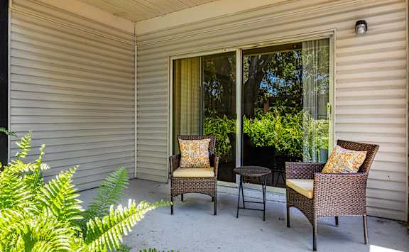 Two chairs and a table are on a porch.