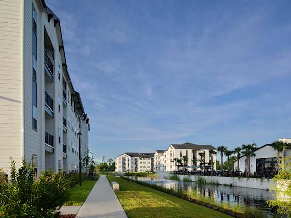 A walkway with grass on either side leads to a building with a waterfront.