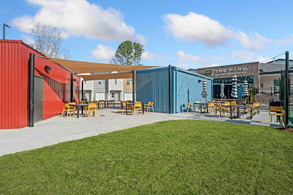 A brightly colored building with a red and blue exterior and a sign that reads "The Parl" sits next to a grassy area with picnic tables.
