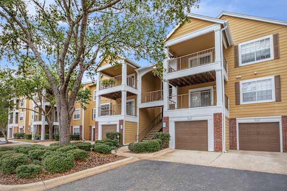 A two-story apartment building with a garage door and a tree in front.