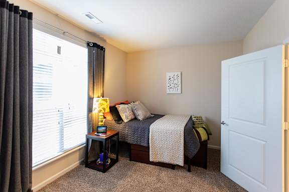 A bedroom with a bed, nightstand, and window with curtains.