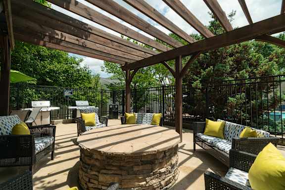 A wooden pergola over a stone fire pit with yellow cushions.