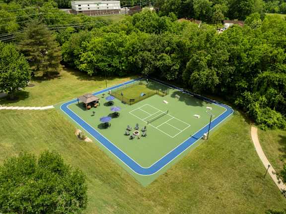 A tennis court surrounded by trees and a building in the background.