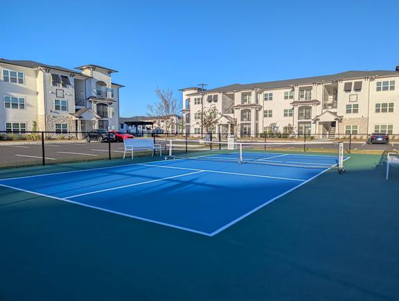 A blue tennis court in front of apartment buildings.