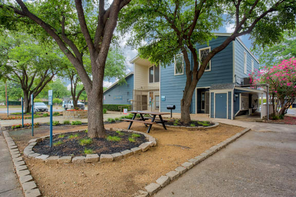 a picnic table in front of a blue house with trees