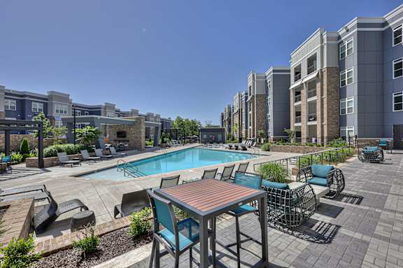 A pool area with a table and chairs in front of apartment buildings.