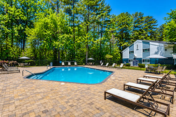 A pool surrounded by trees and lounge chairs.