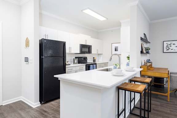 A black refrigerator is in a kitchen with white countertops.