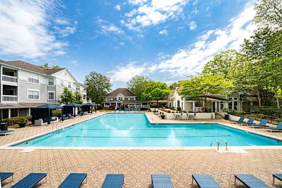 A large swimming pool surrounded by blue lounge chairs and apartment buildings.