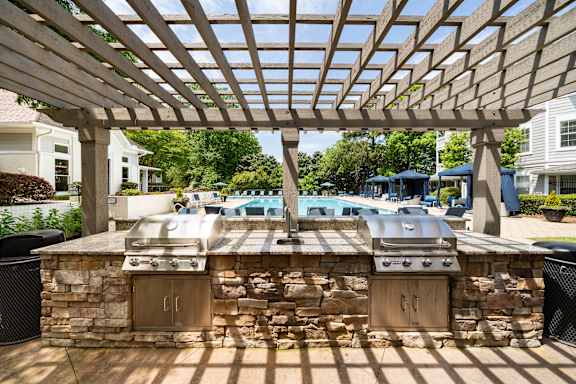 A grill is built into a stone wall under a wooden pergola.