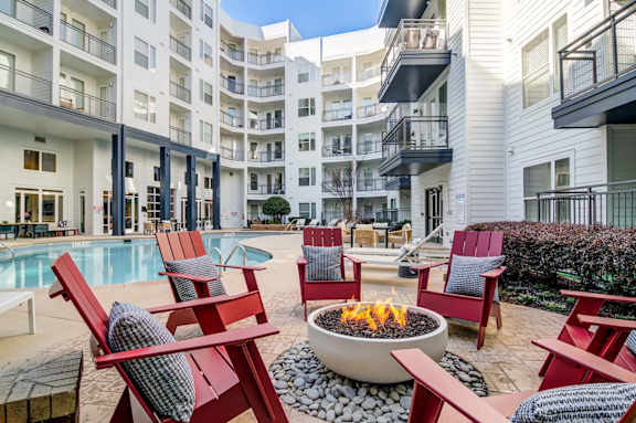 A fire pit sits in the middle of a patio surrounded by red chairs.
