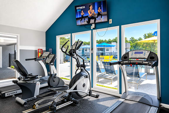 A fitness room with treadmills, elliptical machines, and a television showing a fitness program.