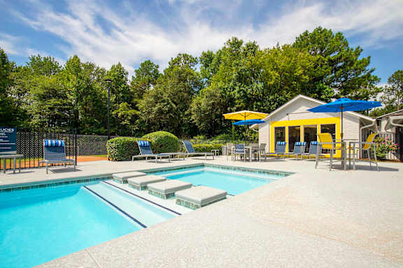 A pool with a yellow building and trees in the background.