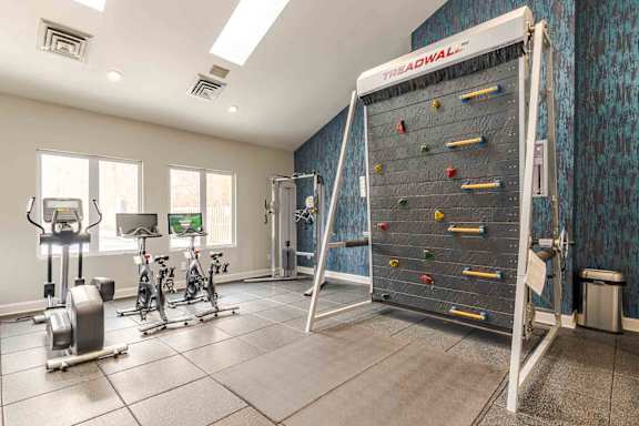A room with a wall-mounted climbing wall, exercise bikes, and a treadmill.