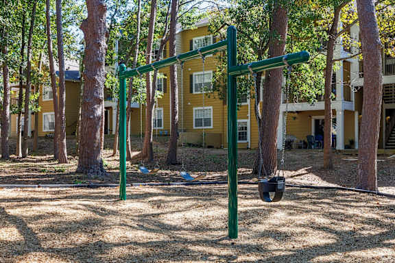 A playground with a green swing set in front of a yellow building.