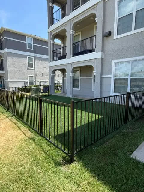 A black metal fence surrounds a grassy area in front of a building.