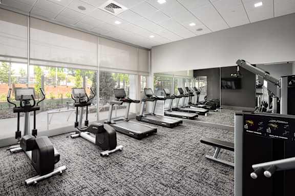 a row of treadmills and exercise machines in a room with large windows at Tower on Tenth Apartments, Birmingham, AL, 35205