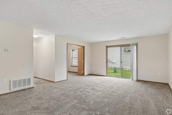 A spacious room with a carpeted floor and a sliding glass door leading to a patio.
