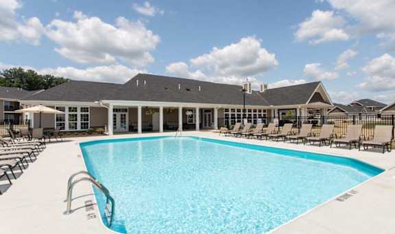 A large swimming pool in front of a building with lounge chairs around it.