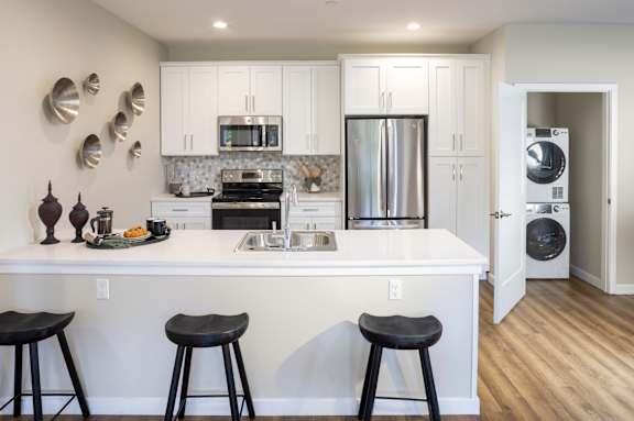 a kitchen with a white counter top with three stools at The Point at Gateways, Yonkers