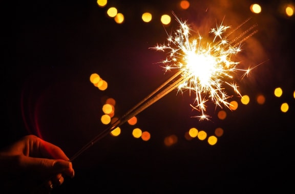 a hand holding a sparkler in front of a dark background