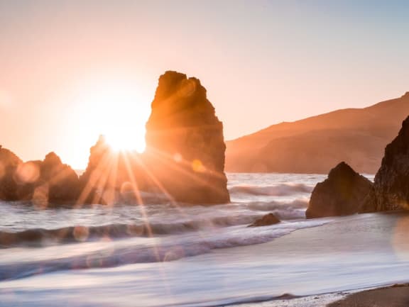 a rock in the ocean with the sunburst behind it