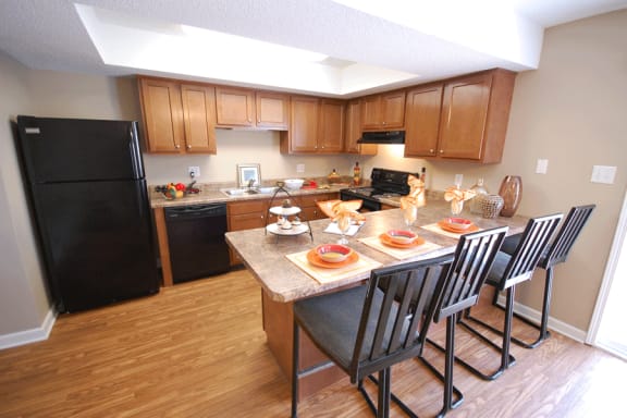 Kitchen with medium wood cabinetry, beige countertops, black appliances with a breakfast bar.  Breakfast bar is set with place settings and 4 chairs.
