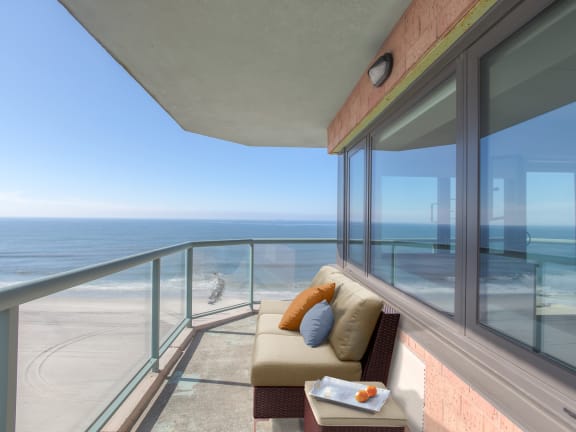 A balcony with a couch and a tray of food overlooking the beach at 10 West Apartments, Long Beach, New York